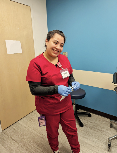 Bianca Morales in crimson scrubs, wearing blue gloves, head tilted to the right