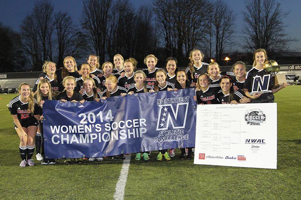The 2014 women's soccar team poses on the field with a championship banner.