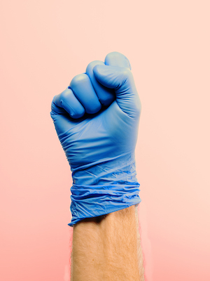 logan maruszak- photo of a closed fist with a blue latex glove stretched over it on a pink ground.