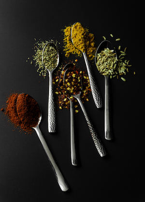 Alyssa Falk- five spoons with different brightly colored spices on a black background.